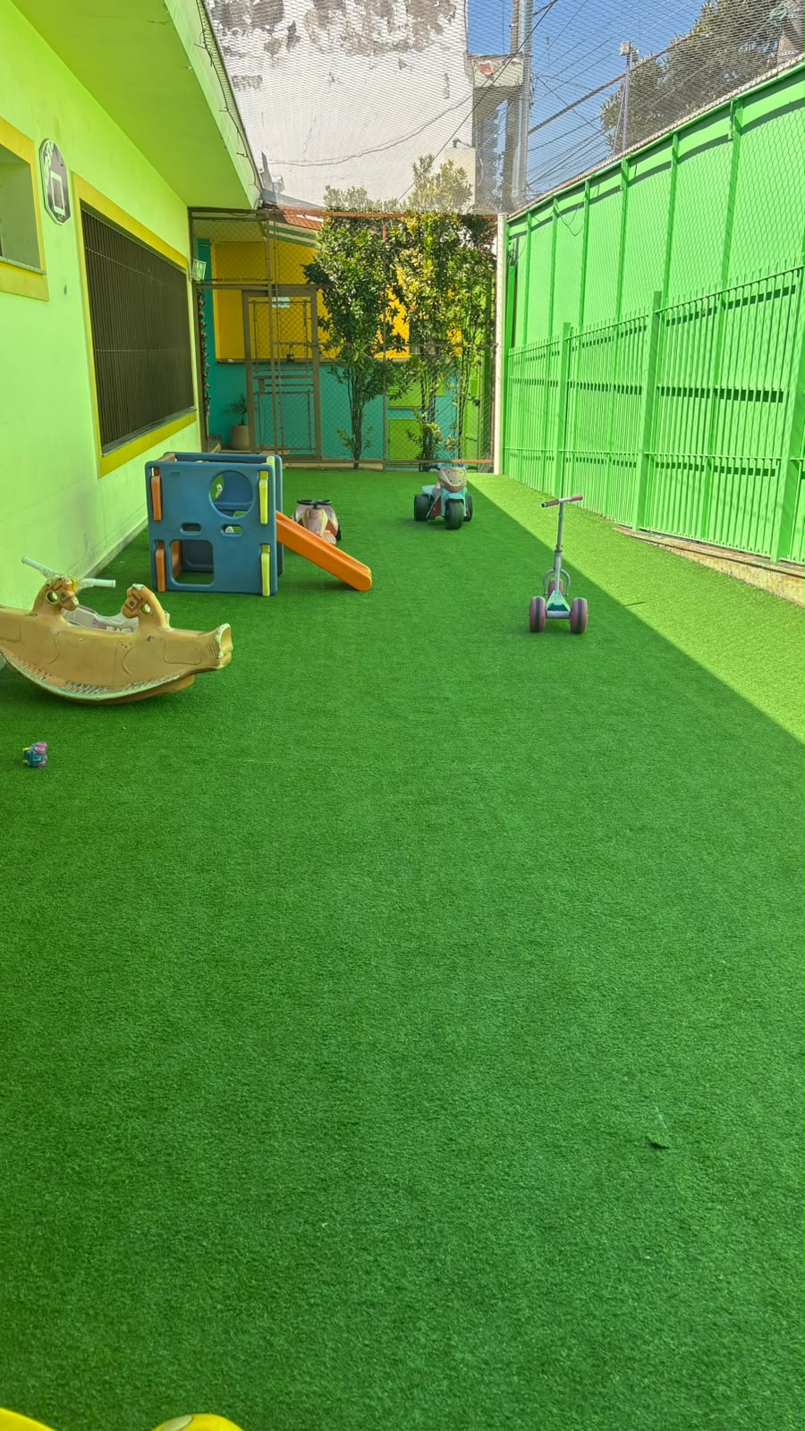 Corredor externo da RUAH com triciclos e patinete sobre a grama sintética